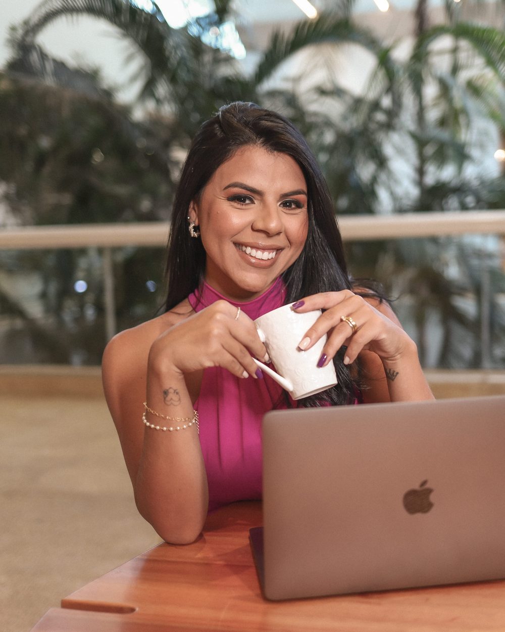 Thais Lasse sorrindo com uma xícara em frente ao notebook